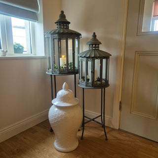 Set of 2 Heritage Lanterns from Lily Bloom with distressed grey-green finish, featuring large (H:1300mm) and small (H:1070mm) lanterns. Ideal for candles or fairy lights. Available at www.lilybloom.ie.